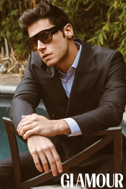 Model Andrea Denver in a dark blazer and tinted sunglasses seated by a pool for Glamour Man Bulgaria.
