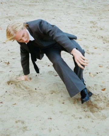 Model Marnix Eyckmans wearing a charcoal grey suit and black tie posing dynamically on sand.