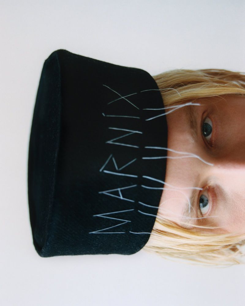 Close-up of a fair-skinned adult wearing a black beanie with the brand name 'Marnix' in white, set against a plain white background.