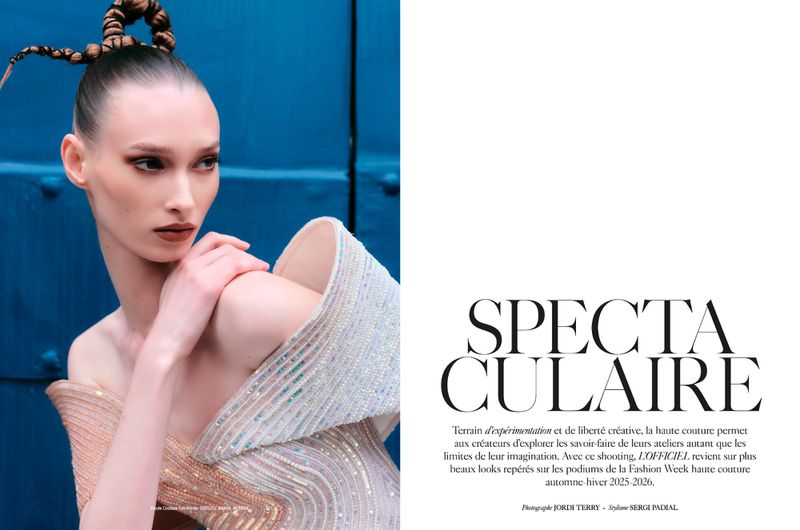 Fashion editorial shot of an adult female model wearing a formal dress with a blue wall background and unique braided hairstyle.