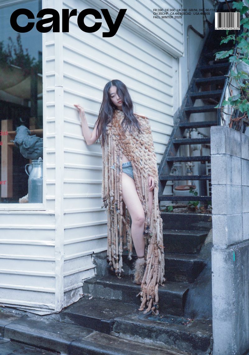 Magazine cover photo of a young woman with long dark hair wearing a long, fringed beige shawl and standing on outdoor steps.