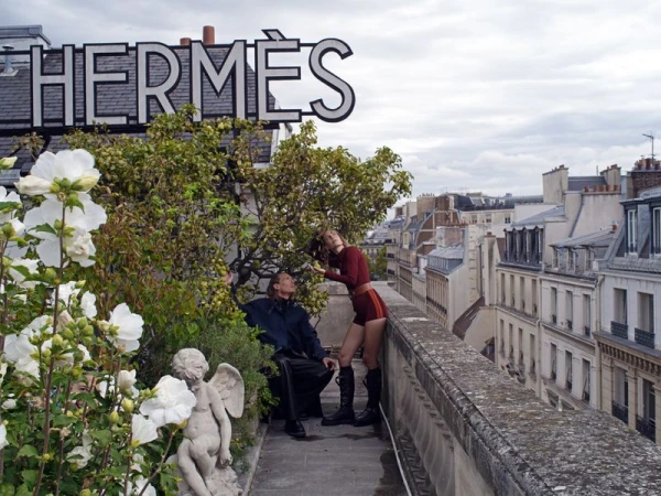 Fashion shoot on a rooftop featuring a man and a woman with the Hermès logo in the background and a cityscape in the distance.