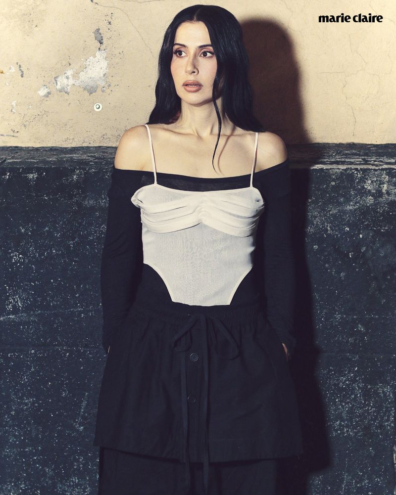 A striking image of a brunette woman in a black and white outfit, posing against a textured wall with Marie Claire logo in the corner.