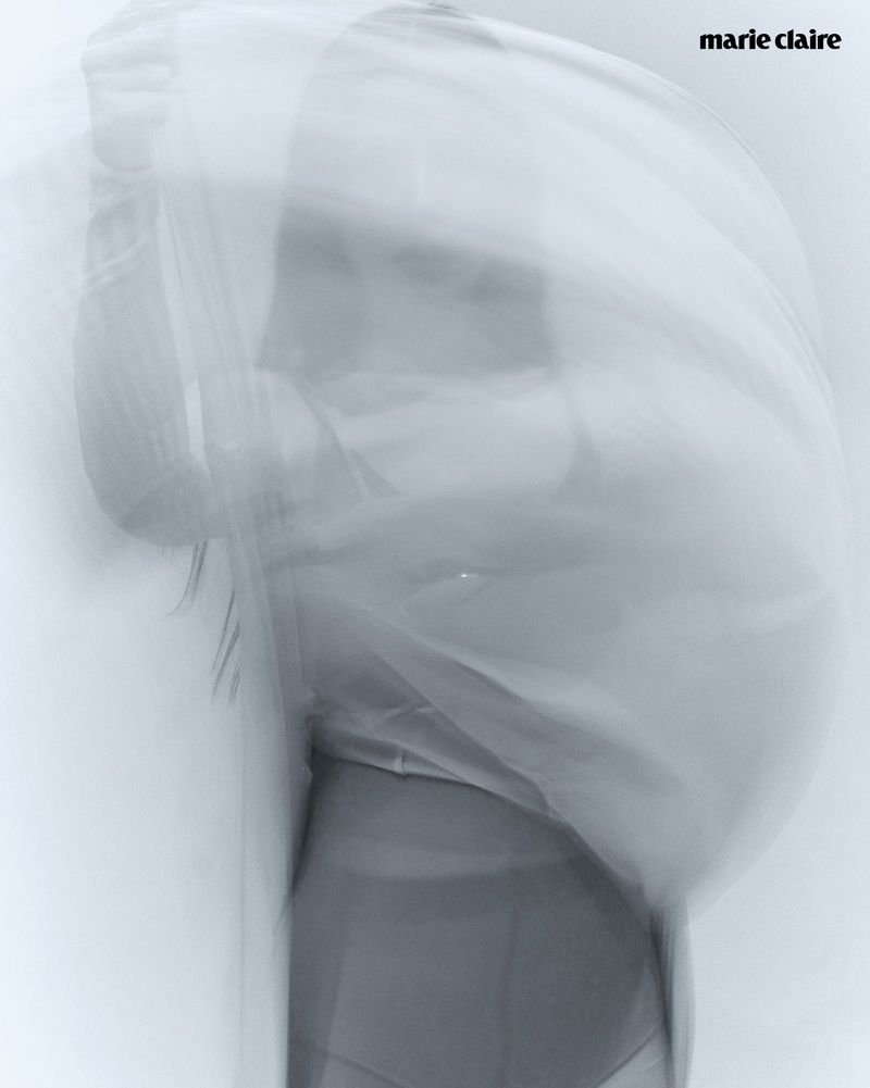Monochromatic fashion photography of a blurry figure. Abstract image, white background, motion blur, neutral tones, magazine logo.
