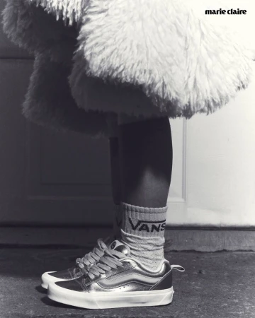 Close-up black and white shot of a person wearing metallic sneakers and socks, with part of a fluffy coat in the background.