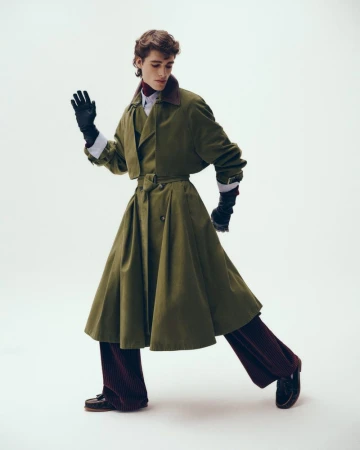 Model Theo Crown posing in a flared olive green trench coat and burgundy corduroy trousers against a white backdrop.