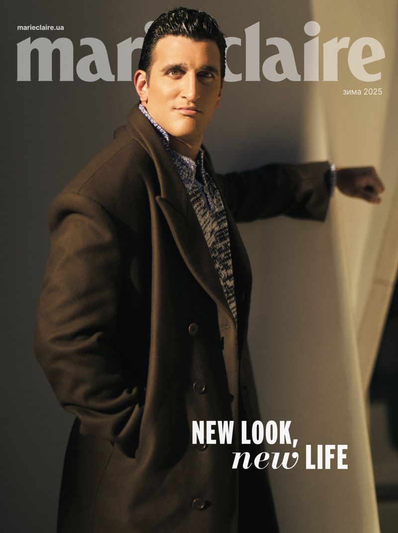 Magazine cover featuring an adult male wearing a dark coat standing next to a light colored wall. The magazine name is at the top.