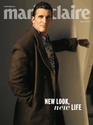Man wearing a brown coat and patterned shirt posing against a wall for a digital magazine cover with bold text overlays.