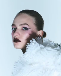 Close-up beauty portrait of a woman wearing dark glossy lipstick, winged eyeliner, and an oversized textured white petal collar.
