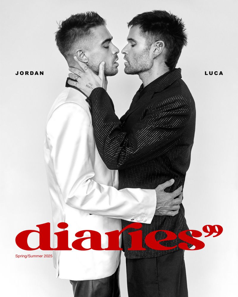 Two adult men in stylish blazers pose closely together in a bright photo studio. One man's hand rests on the other's neck. Red text overlay.