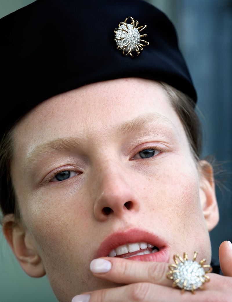 Close-up portrait of a fair-skinned adult woman wearing a black beret adorned with a jeweled pin and a matching ring.