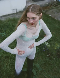 Model in white lace bodysuit and dark boots standing on grass for Glass Magazine editorial