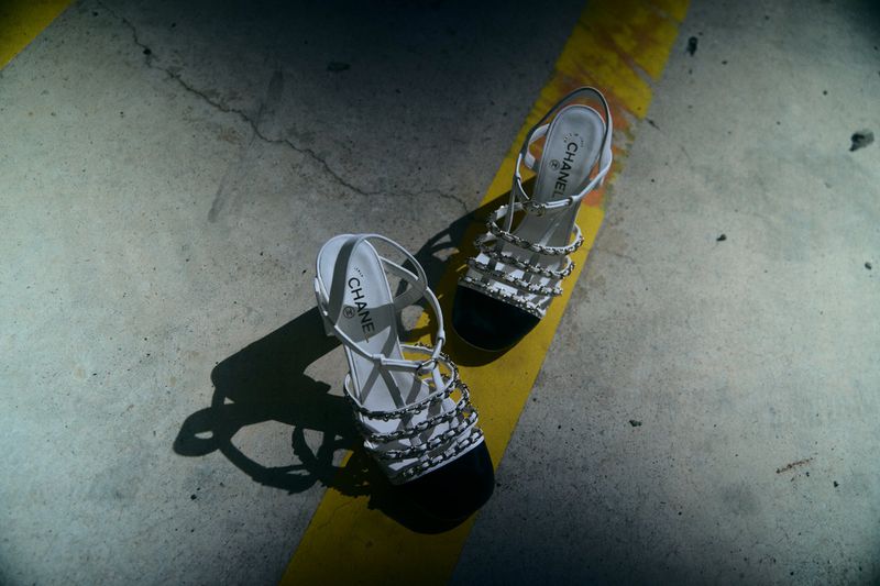 Two Chanel slingback heels with black toe caps and white straps on a yellow-striped gray concrete surface under moody lighting.