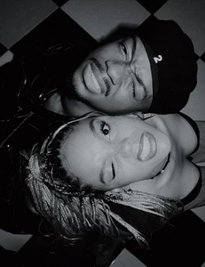 Monochrome overhead portrait of a Black man and woman making expressive faces while lying on a checkered floor.