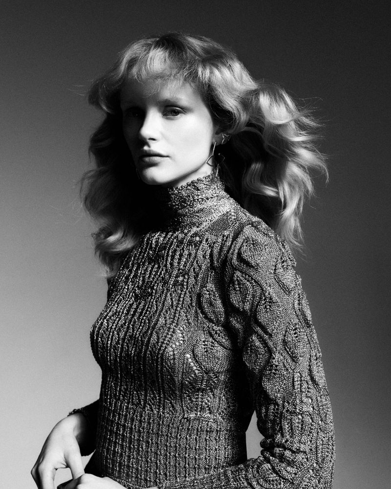 Monochrome portrait of Emma Laird wearing a high-neck textured knit sweater against a gradient studio background.