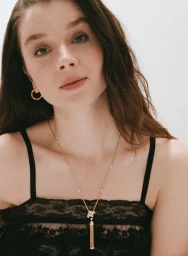 Portrait of Claudia Jessie wearing a black lace camisole top, gold tassel pendant necklace, and hoop earrings against a white studio wall.