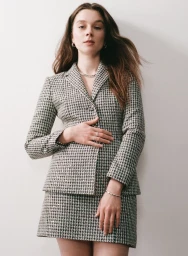 Claudia Jessie wearing a grey houndstooth blazer and matching mini skirt against a white studio background.