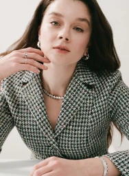 Claudia Jessie wearing a houndstooth tweed blazer with silver and gemstone jewellery against a pale background.