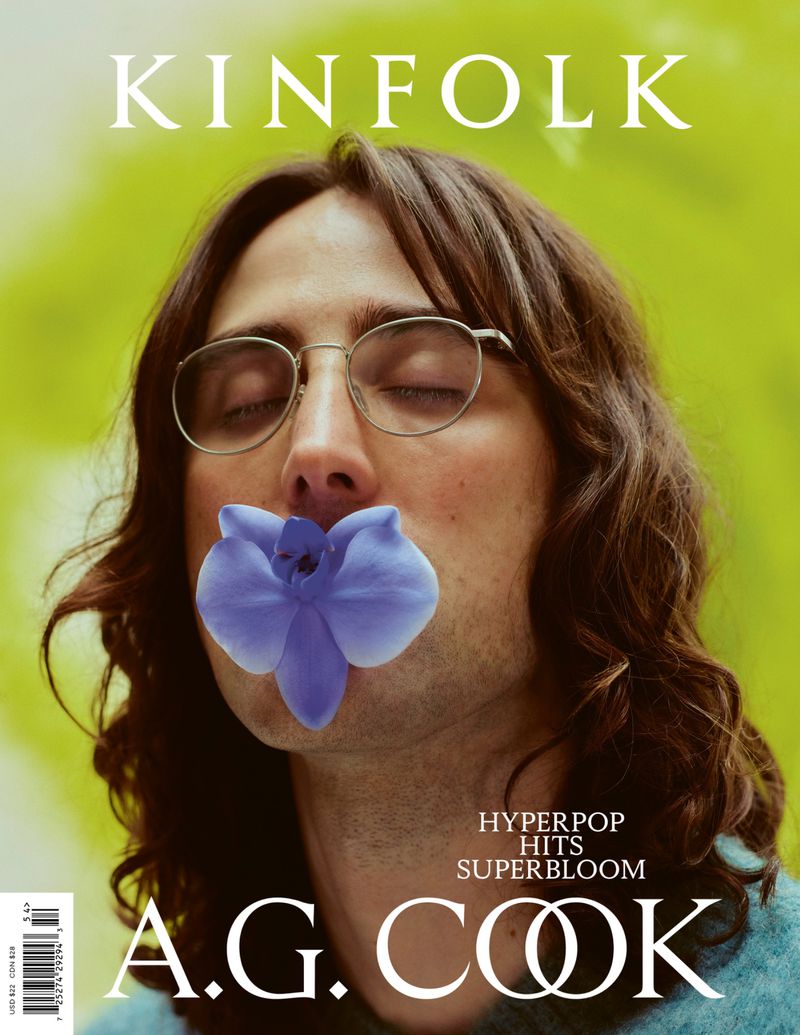 Magazine cover featuring A. G. Cook with an orchid covering their mouth, wearing glasses, and a green background with the Kinfolk logo.