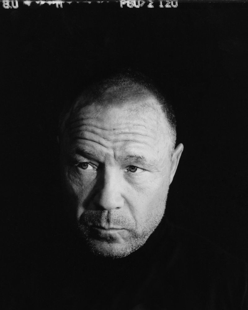 Striking black and white portrait of a mature man with a serious expression, captured with dramatic lighting and a close-up perspective.