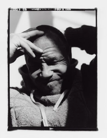 Black and white portrait of adult male in a hooded sweatshirt with hand on head, partially shadowed against a light background.