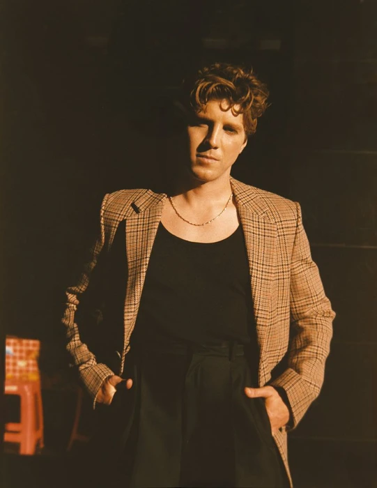 Lukas Gage in a plaid blazer and black tank top against a dark background for Glass Man