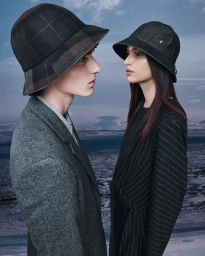 Two models wearing bucket hats and tailored outerwear against a cloudy horizon backdrop for Helen Kaminski Fall 24.