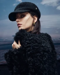 Model wearing a black textured cap and fluffy black coat against an overcast sky background for Helen Kaminski