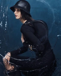 Model wearing black leather bucket hat and black clothing against textured dark blue background