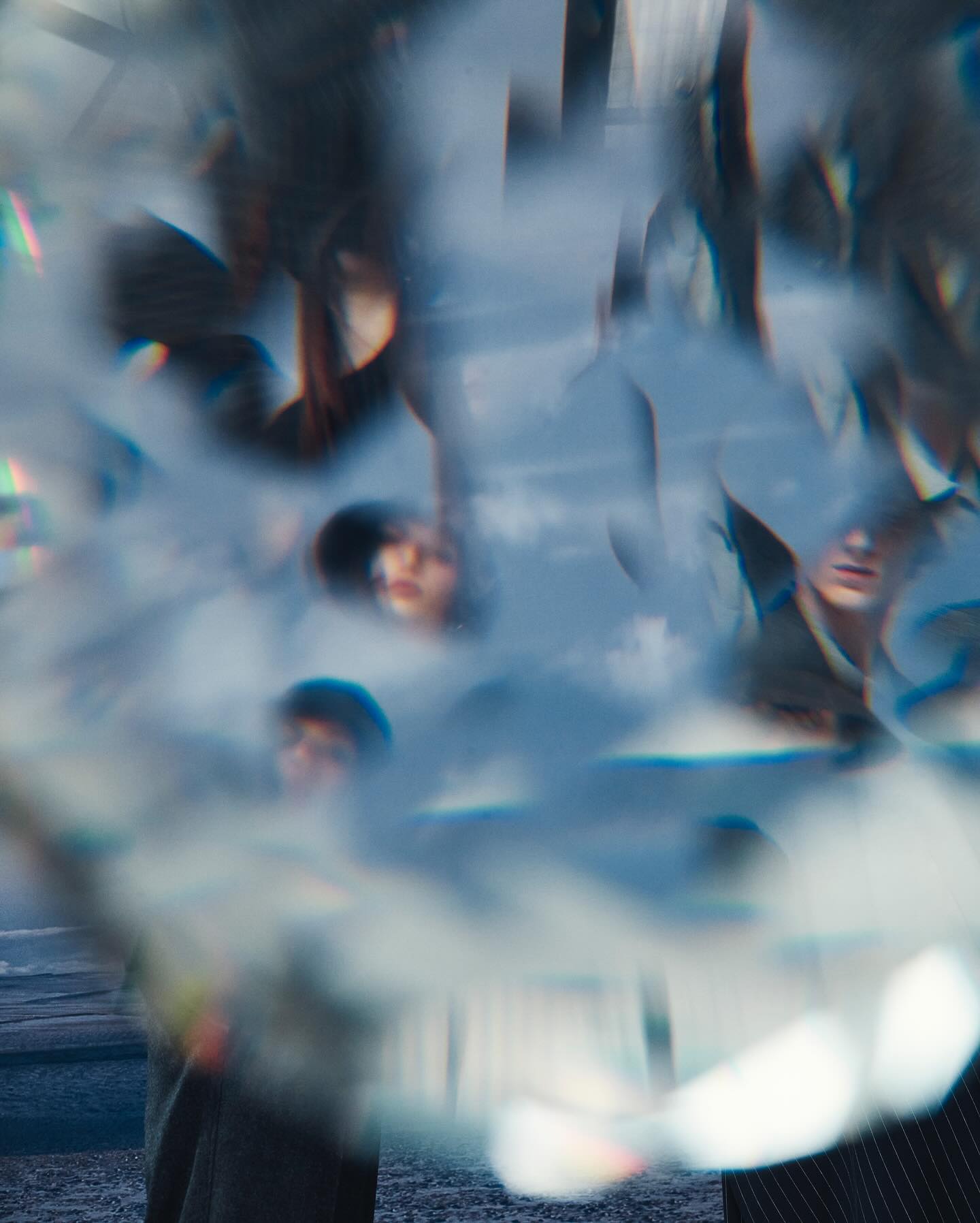 Abstract, blurred image of multiple people with fair skin and dark hair, wearing casual clothing, against a blue sky and blurred background.