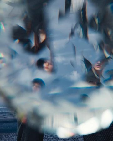 Abstract, blurred image of multiple people with fair skin and dark hair, wearing casual clothing, against a blue sky and blurred background.