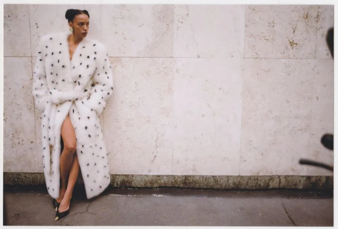 Elegant woman in a patterned white coat poses against a textured wall, showcasing fashion and style, highlighting her sophistication.