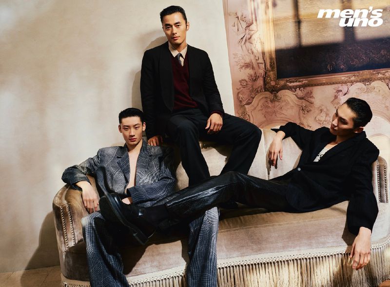 Three Asian male fashion models pose indoors on an ornate sofa in suits for a studio shot from a men's magazine cover.