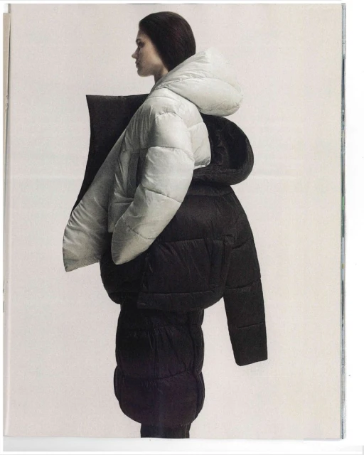 Fashion shot of a woman in a white hooded puffer jacket worn over a black puffer jacket against a pale backdrop in a magazine.