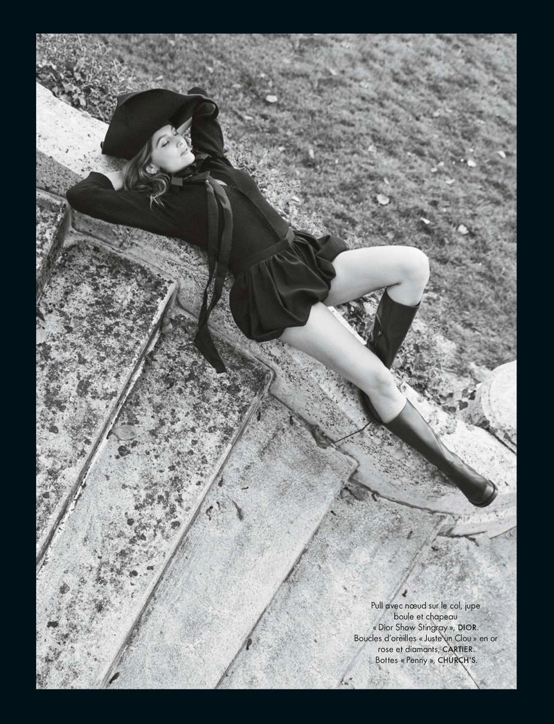 Black and white portrait of a woman in a floppy hat and dress reclining on stone steps, with a grassy slope in the background.