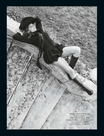 Black and white portrait of a woman in a floppy hat and dress reclining on stone steps, with a grassy slope in the background.