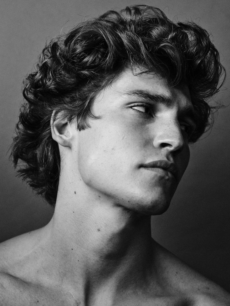 Striking black and white portrait of a young adult male with curly dark hair, gazing to the side, showcasing classic portraiture.