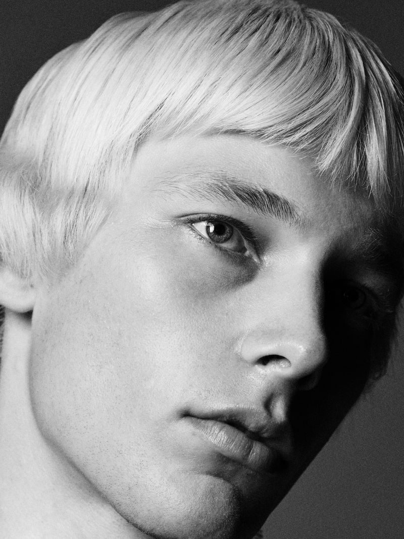 Black and white close-up portrait of model Maxime Laval with a cropped bowl haircut and serious expression.