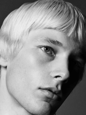 Black and white close-up portrait of model Maxime Laval with a cropped bowl haircut and serious expression.