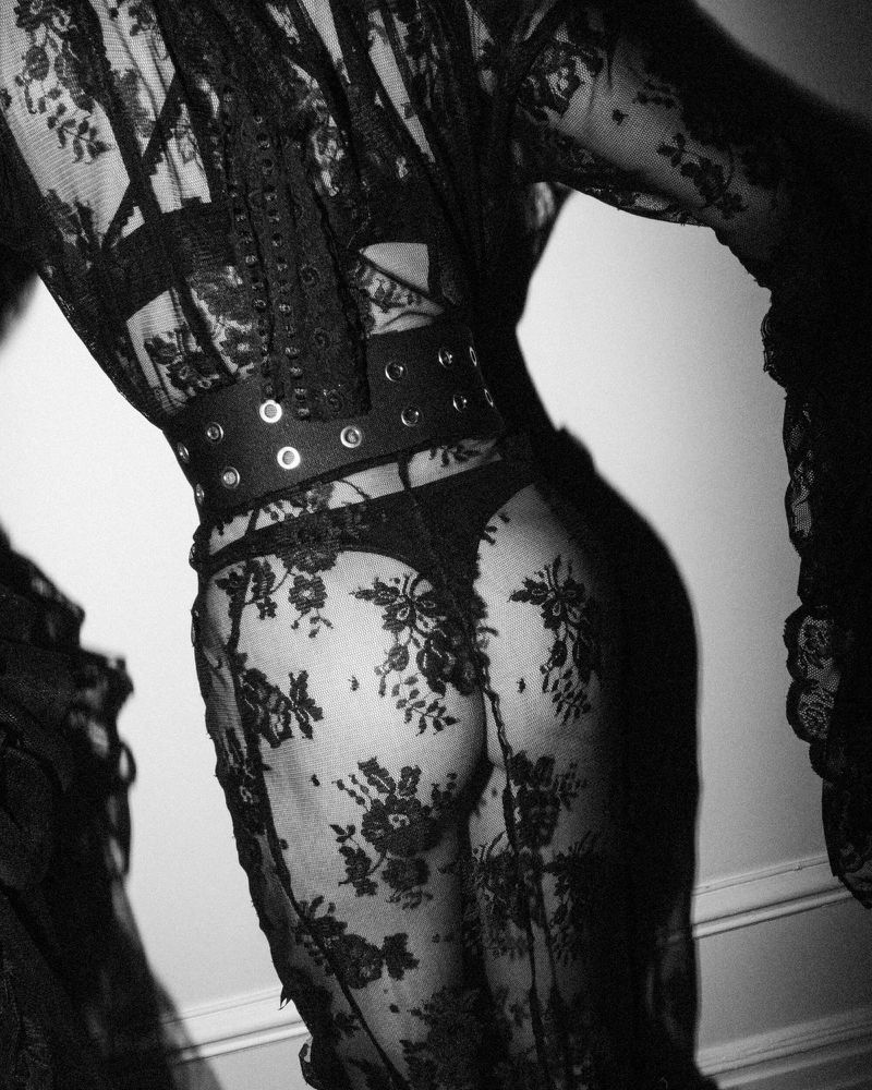Back view of a person wearing a black lace dress and corset, showcasing fashion and body positivity in a grayscale aesthetic.