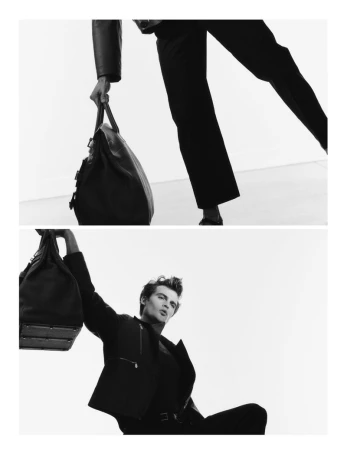 Monochrome shot of a man in a suit holding a leather duffel bag in a bright, minimalist setting. Fashionable and stylish.