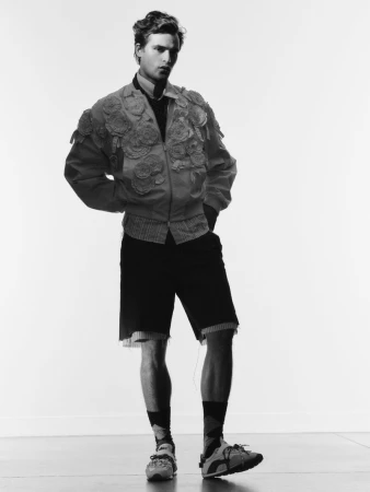 Black and white fashion portrait of a young adult man in a floral jacket and shorts against a white background, shot in a studio.