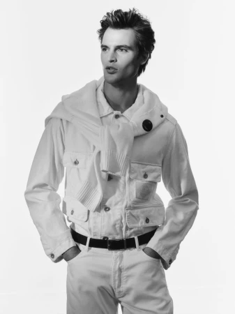 Black and white medium shot of a male model in a white outfit with sweater draped over his shoulders in a white photo studio.