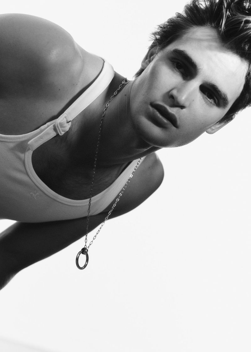 Black and white portrait of an adult male in a tank top, wearing a necklace, against a bright white background.