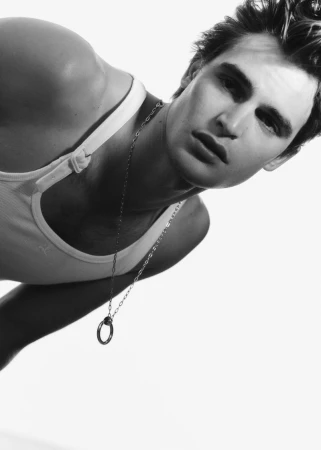 Black and white portrait of an adult male in a tank top, wearing a necklace, against a bright white background.