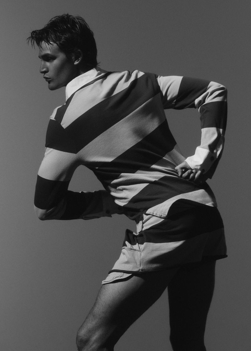 Black and white portrait of a fair-skinned adult male posing with a striped long-sleeved shirt and shorts in a neutral studio setting.