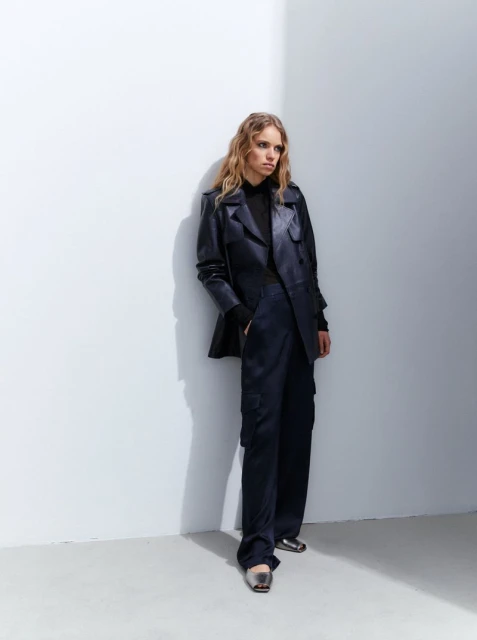 A fashionable adult woman poses in a navy blue suit against a white wall, showcasing modern sophistication in a studio setting.