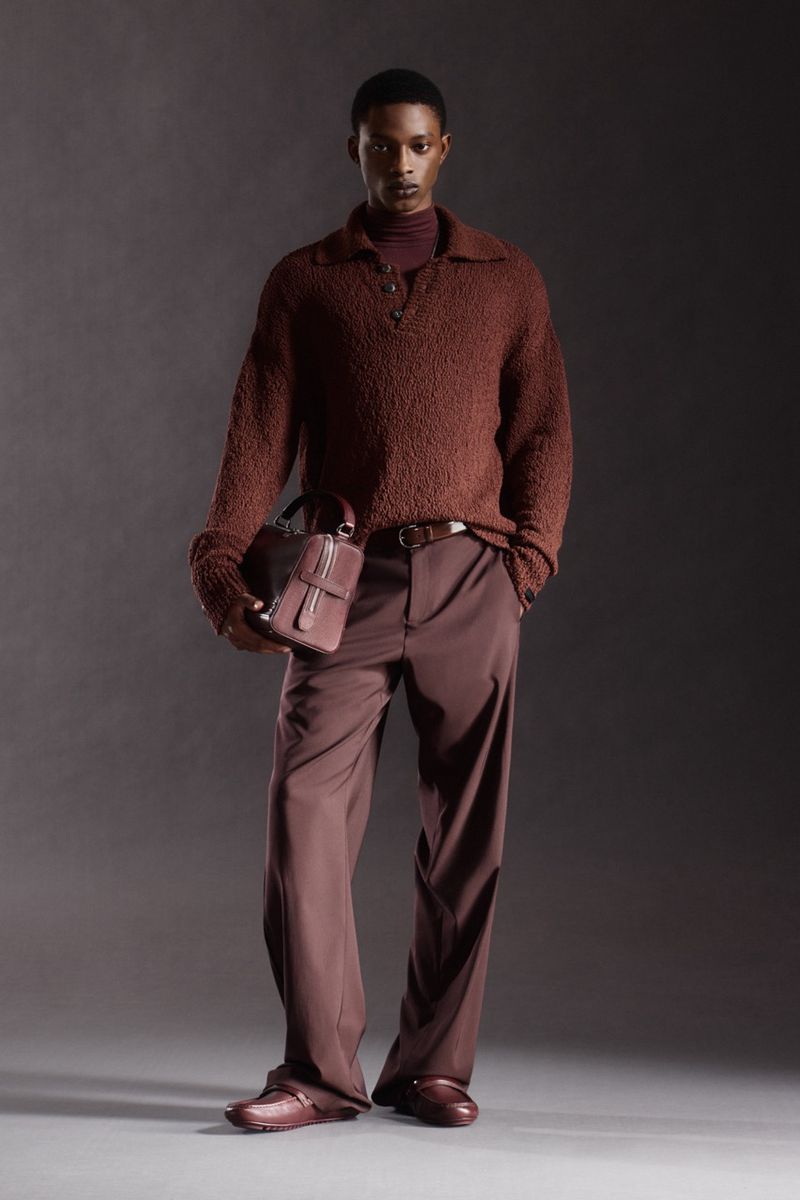 Model Nonso Ojukwu in a brown textured knit polo sweater, wide-leg trousers, and holding a leather bag for Ferrari Pre-Fall 2026.