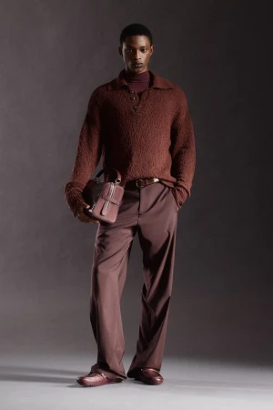 Model Nonso Ojukwu in a brown textured knit polo sweater, wide-leg trousers, and holding a leather bag for Ferrari Pre-Fall 2026.