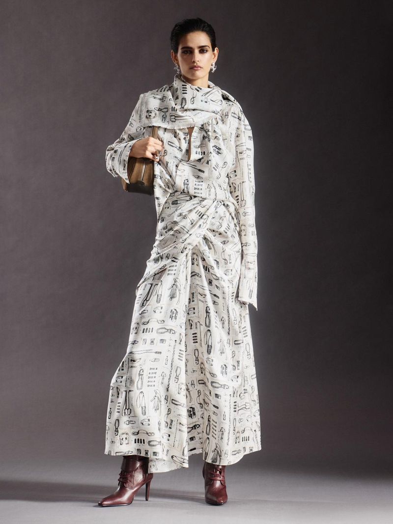 Full-length shot of an adult female wearing a printed white two-piece outfit and burgundy ankle boots against a grey backdrop.